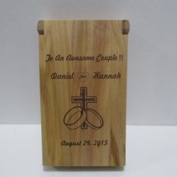 Wooden plaque engraved with "To An Awesome Couple!! Daniel and Hannah, August 29, 2015" and religious symbols.