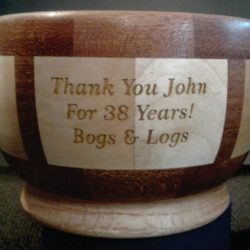A wooden bowl engraved with "Thank You John For 38 Years! Bogs & Logs" on the side.