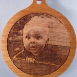 Wooden ornament engraved with a baby’s portrait and the year 2015, featuring a red ribbon loop at the top.