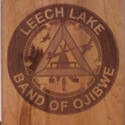 Wooden plaque with the engraved seal of the Leech Lake Band of Ojibwe, featuring an eagle, trees, and traditional symbols.