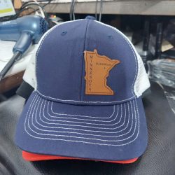 A navy and white trucker hat with a brown Minnesota state patch labeled "Floodwood" on the front.