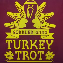 Yellow turkey with six shoes graphic, reads "Gobbler Gang Turkey Trot 2022 5K" on a maroon background with leaf accents.